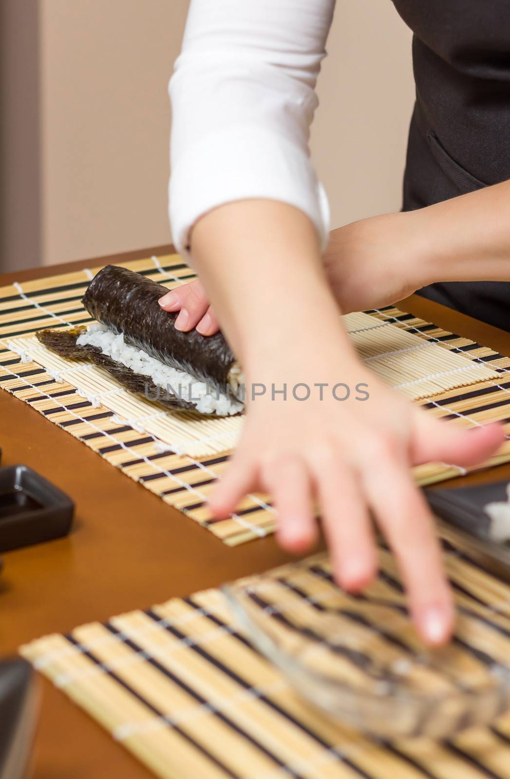 Woman hand moistening with water a edge of japanese sushi to close the roll. Selective focus on the sushi roll