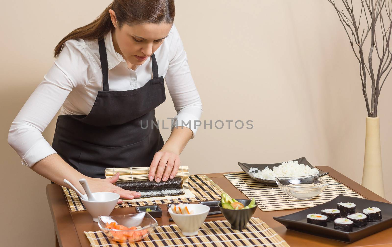 Portrait of woman chef rolling up a japanese sushi with rice, avocado and shrimps on nori seaweed sheet