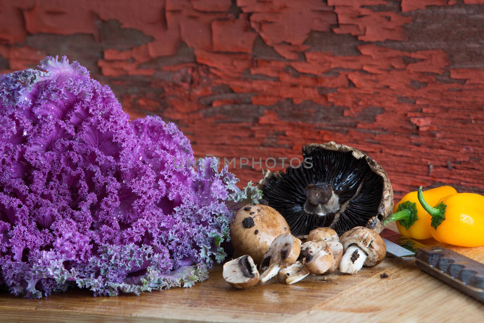 Fresh healthy cooking ingredients with a head of purple curly-leaf kale, fresh agaricus mushrooms and colourful yellow sweet bell peppers in a rustic kitchen on a bamboo cutting board