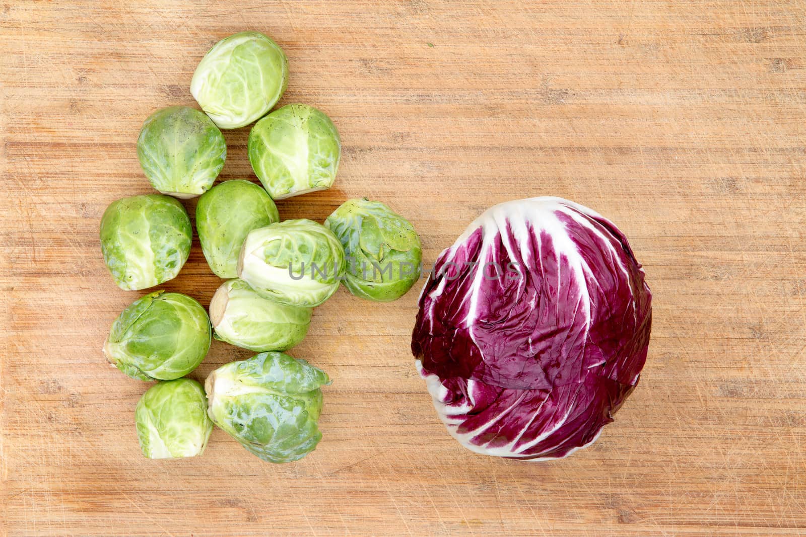 Single cleaned red radicchio with fresh uncooked green brussels sprouts on a bamboo chopping board waiting to be cooked for the evening meal