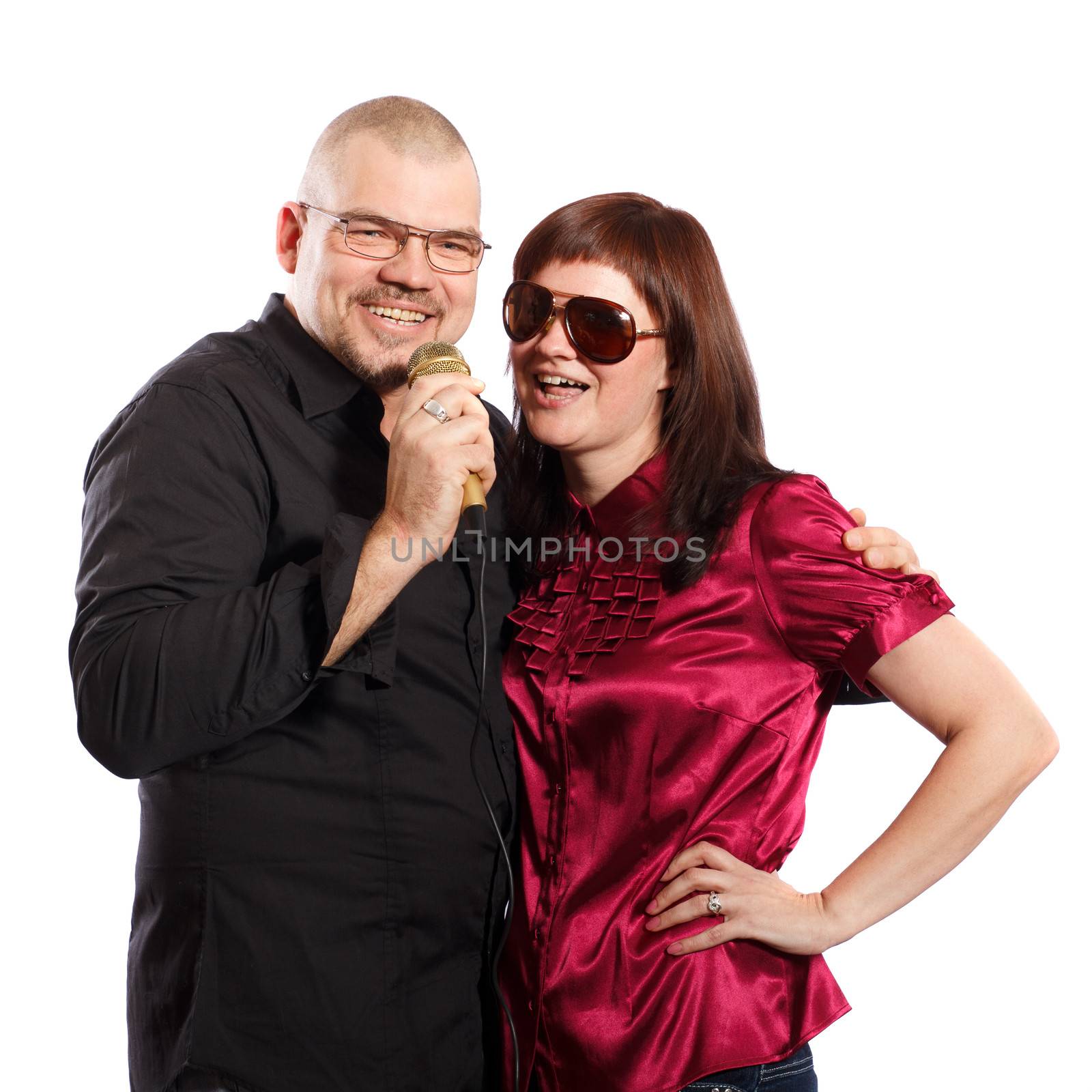 smiling couple sings into a microphone on a white background