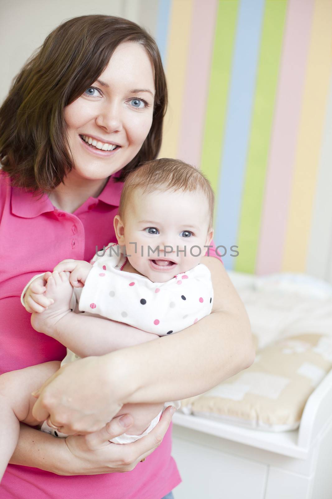 Happy mother holding her baby girl in colorfull room