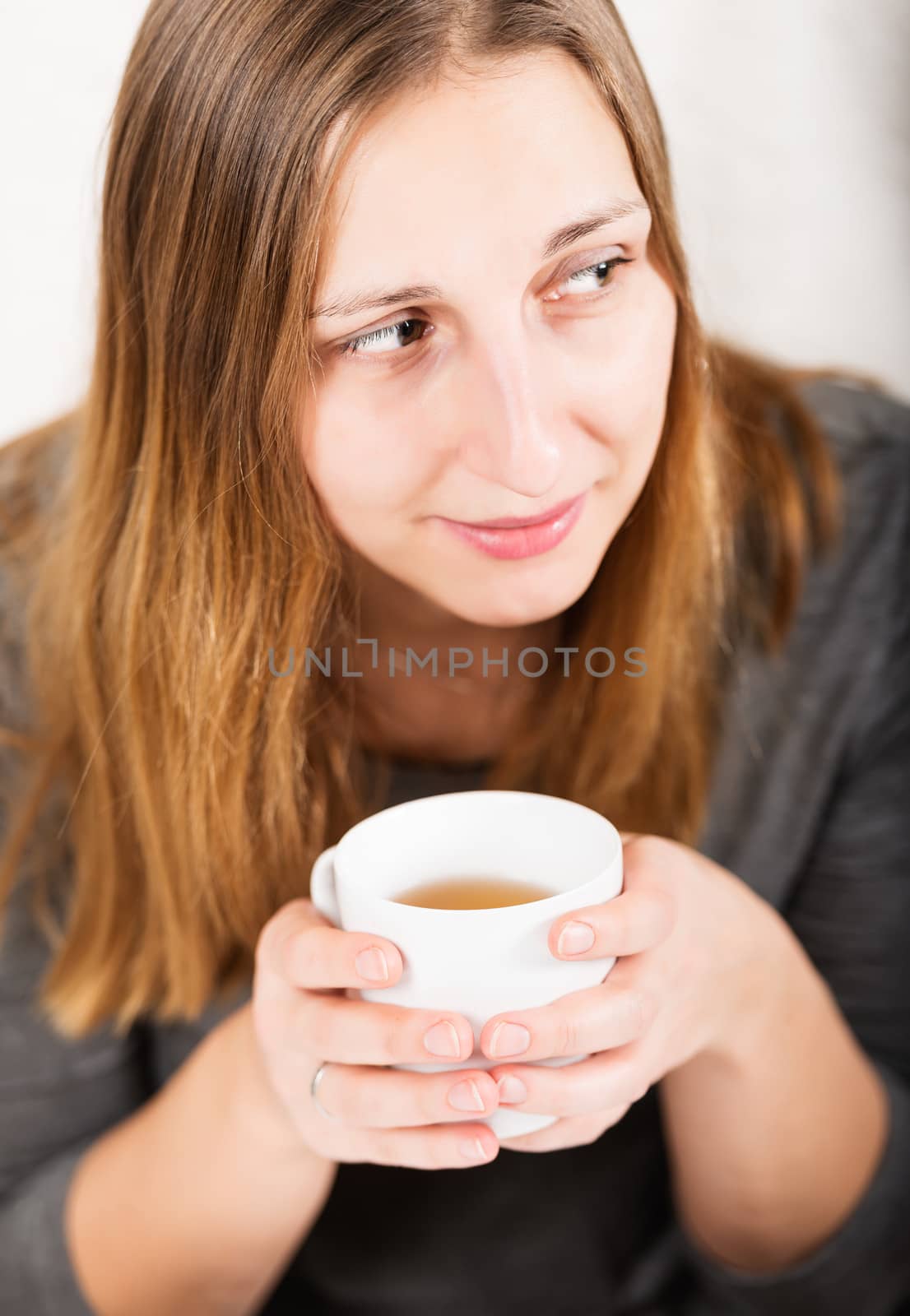 Happy girl in grey holding mug and not looking at camera by Nanisimova