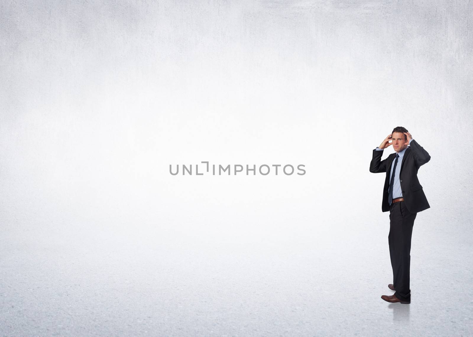 Stressed businessman with hands on head against white wall