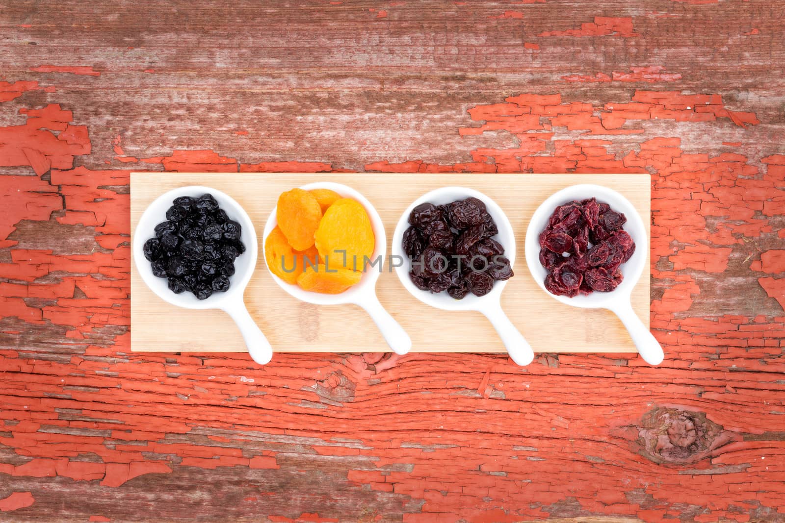 Overhead view of a display on rustic grunge wood of assorted dried berries and fruit in ceramic ramekins with golden apricots, cherries, blueberries and cranberries for a healthy snack or appetizer