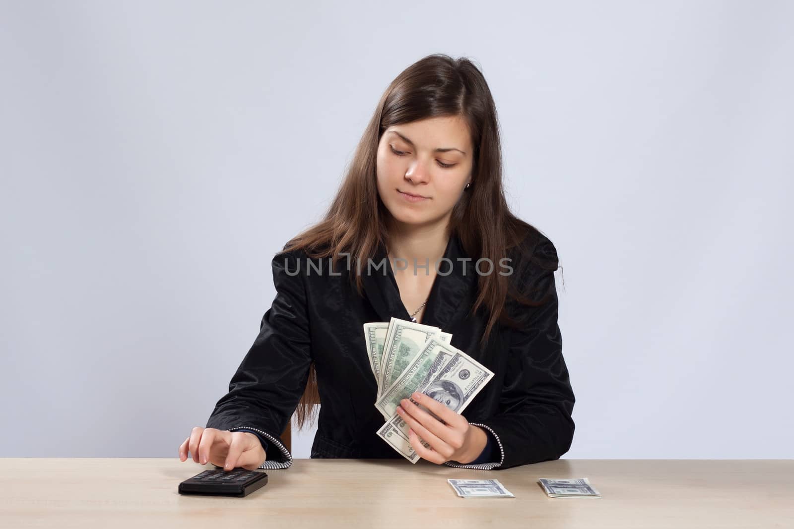 Young long-haired woman sitting at a desk and using a calculator counts dollars