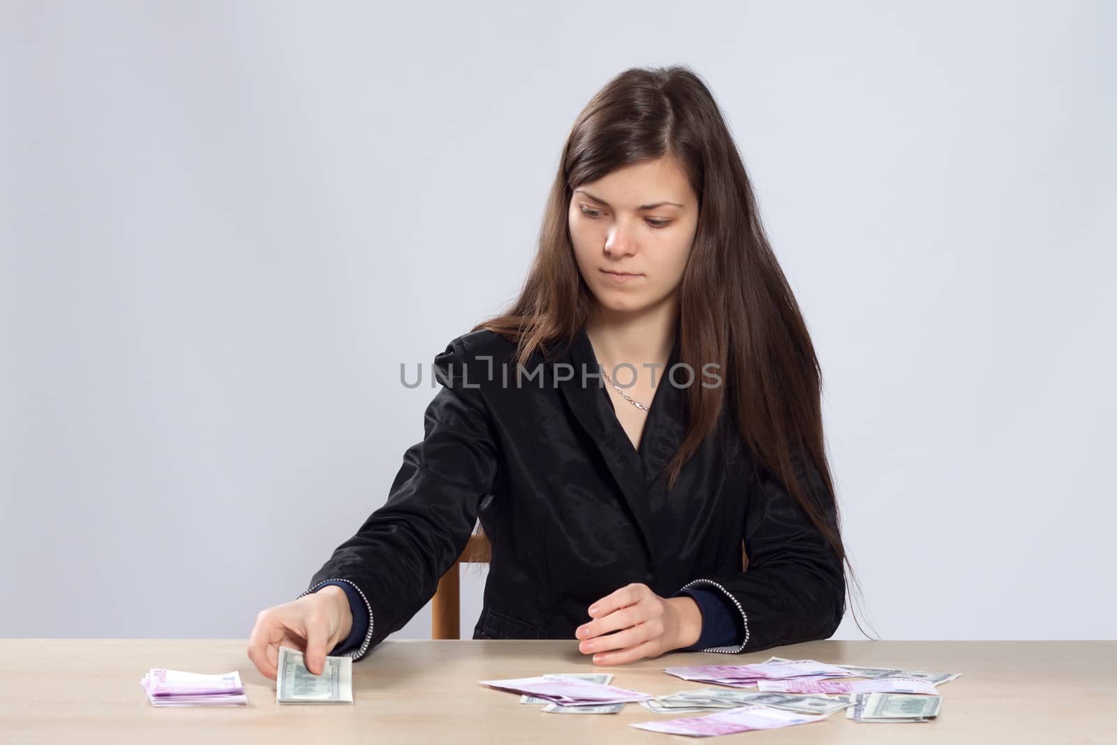 Young long-haired woman sitting at the table and counts euros and dollars and divided them into stacks