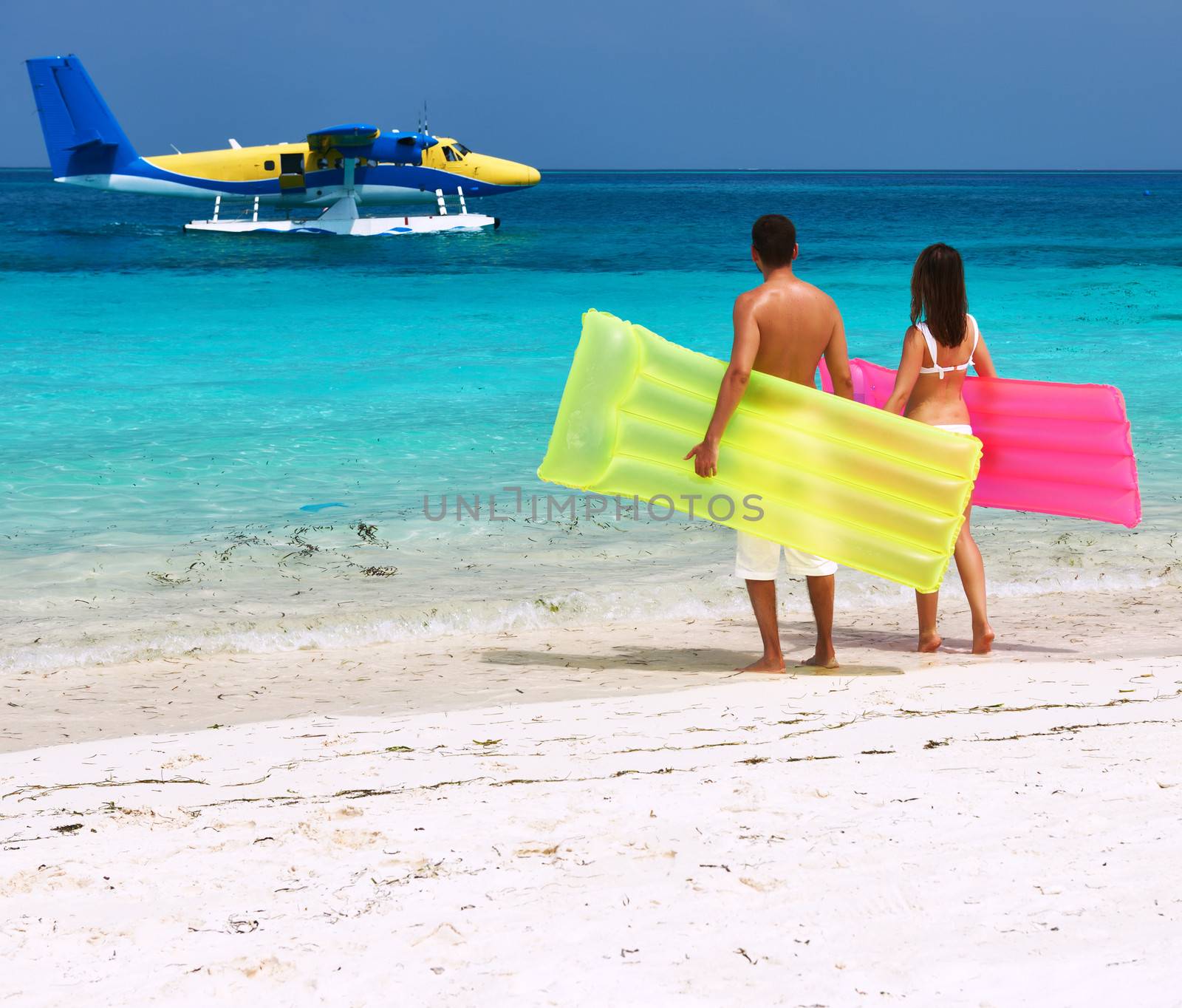 Couple with inflatable rafts looking at arrived seaplane on a tropical beach at Maldives. No brand names or copyright objects