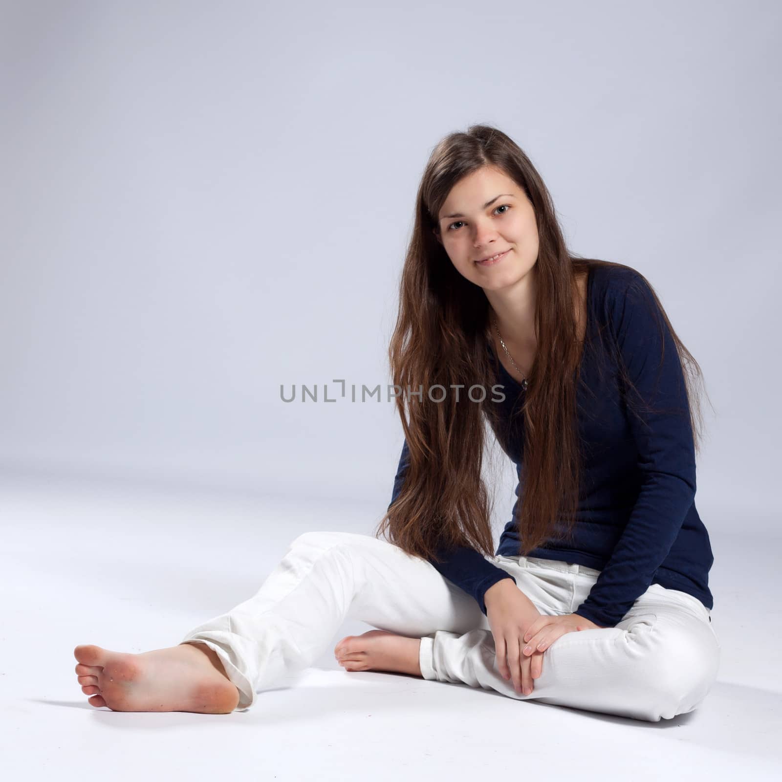 Young long-haired woman without makeup in white jeans and a blue shirt sitting on the floor