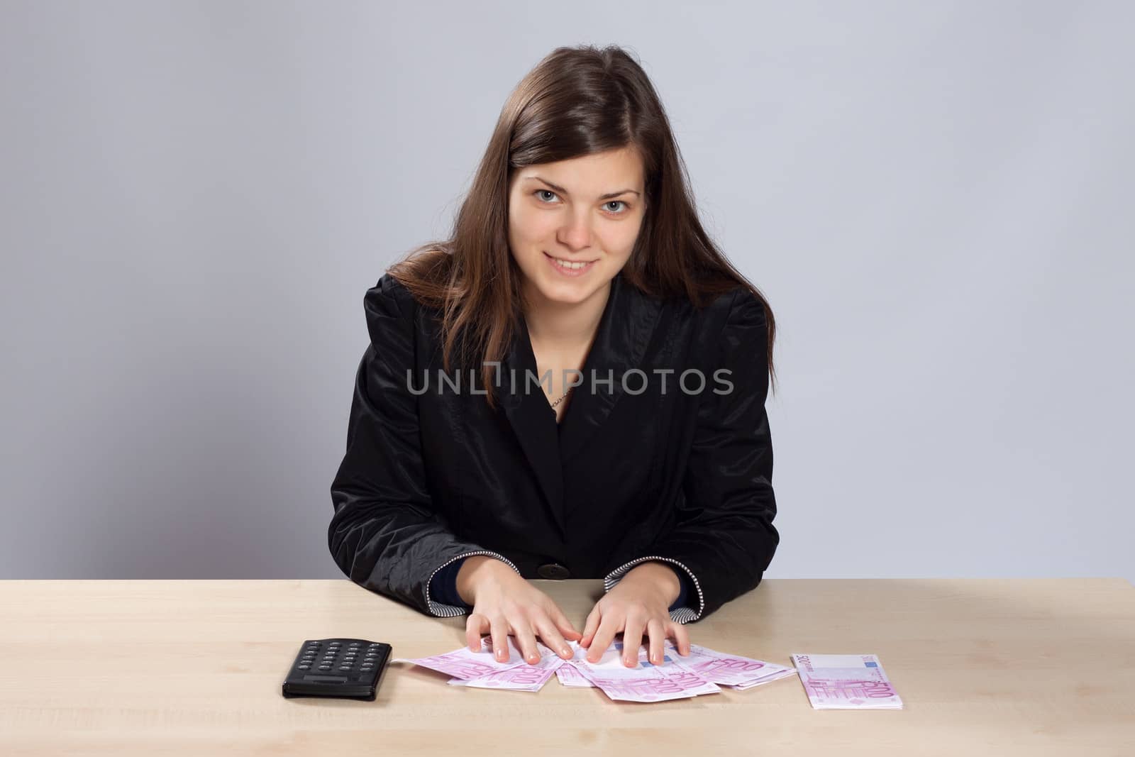 Young long-haired woman sitting at the table and counts using a calculator euros