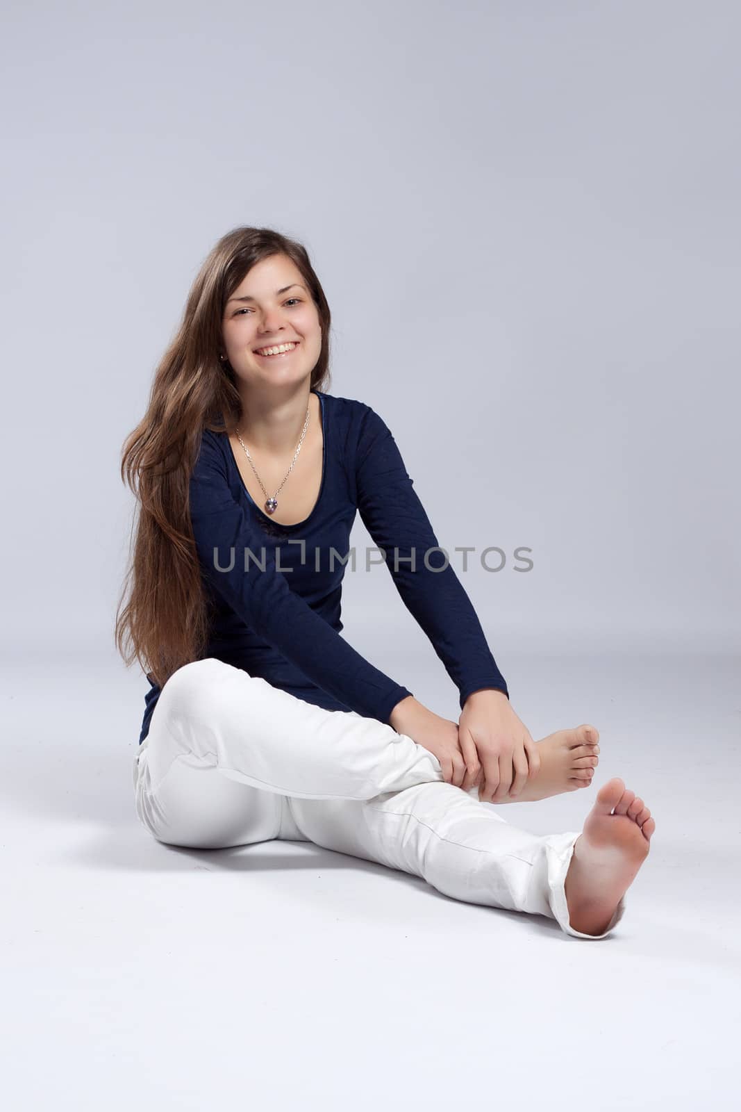 Young long-haired woman without makeup in white jeans and a blue shirt sitting on the floor and laughing