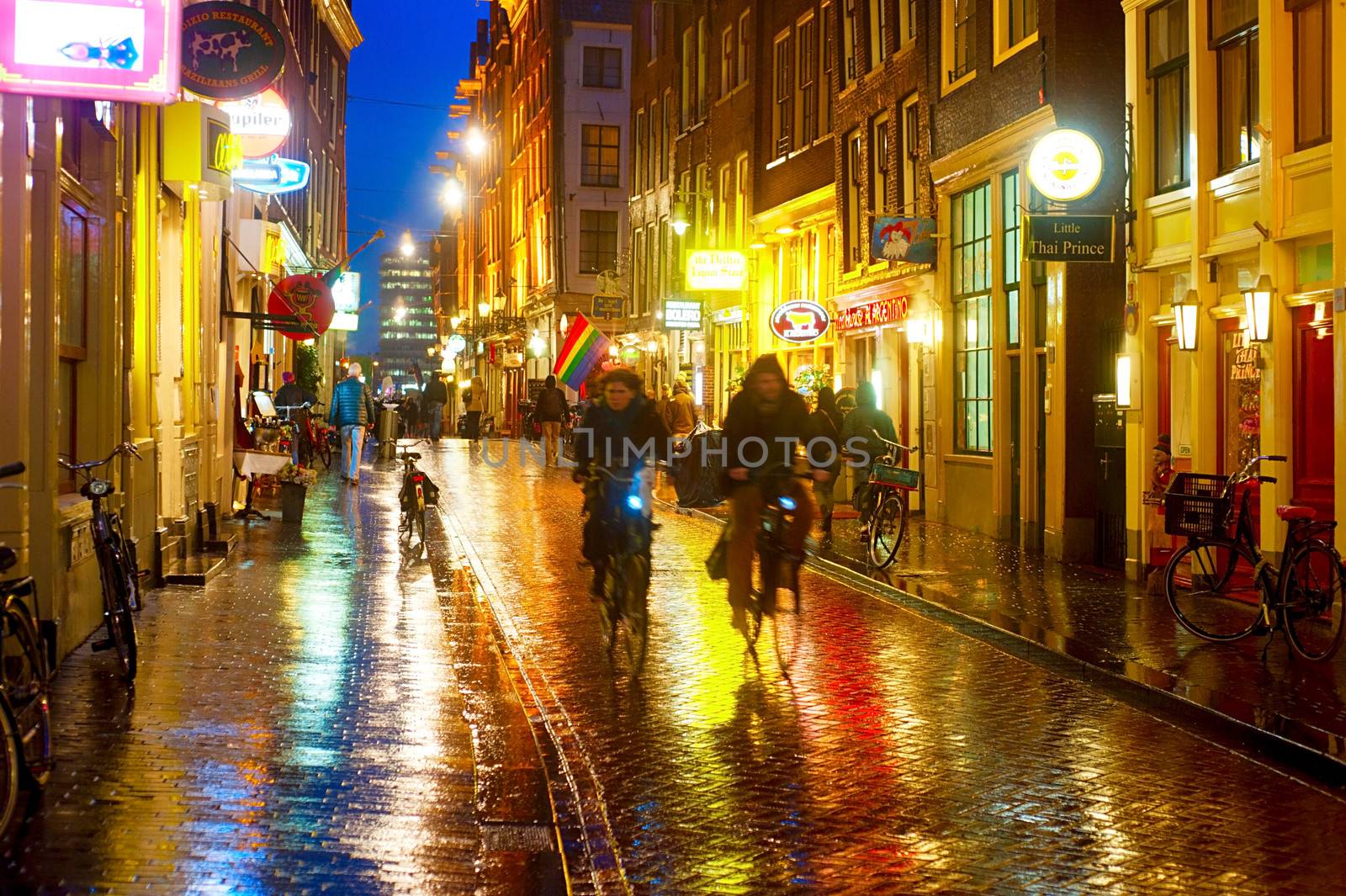 AMSTERDAM, NETHERLANDS - FEB 14, 2014: Unidentified people on the street of an old town of Amsterdam in the evening under the rain.