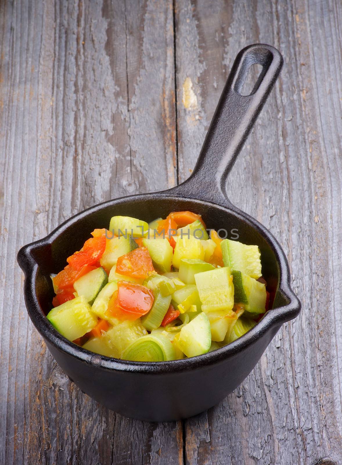 Vegetable Stew with Zucchini in Black Stew Pan isolated on Rustic Wooden background