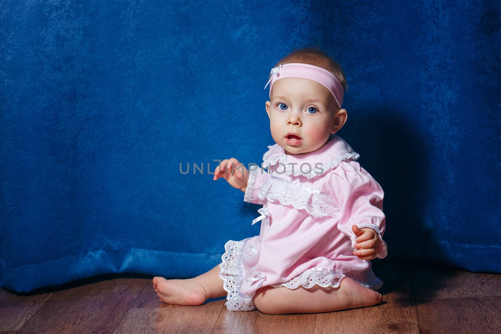 Cute little girl in a pink dress sitting on the floor barefoot