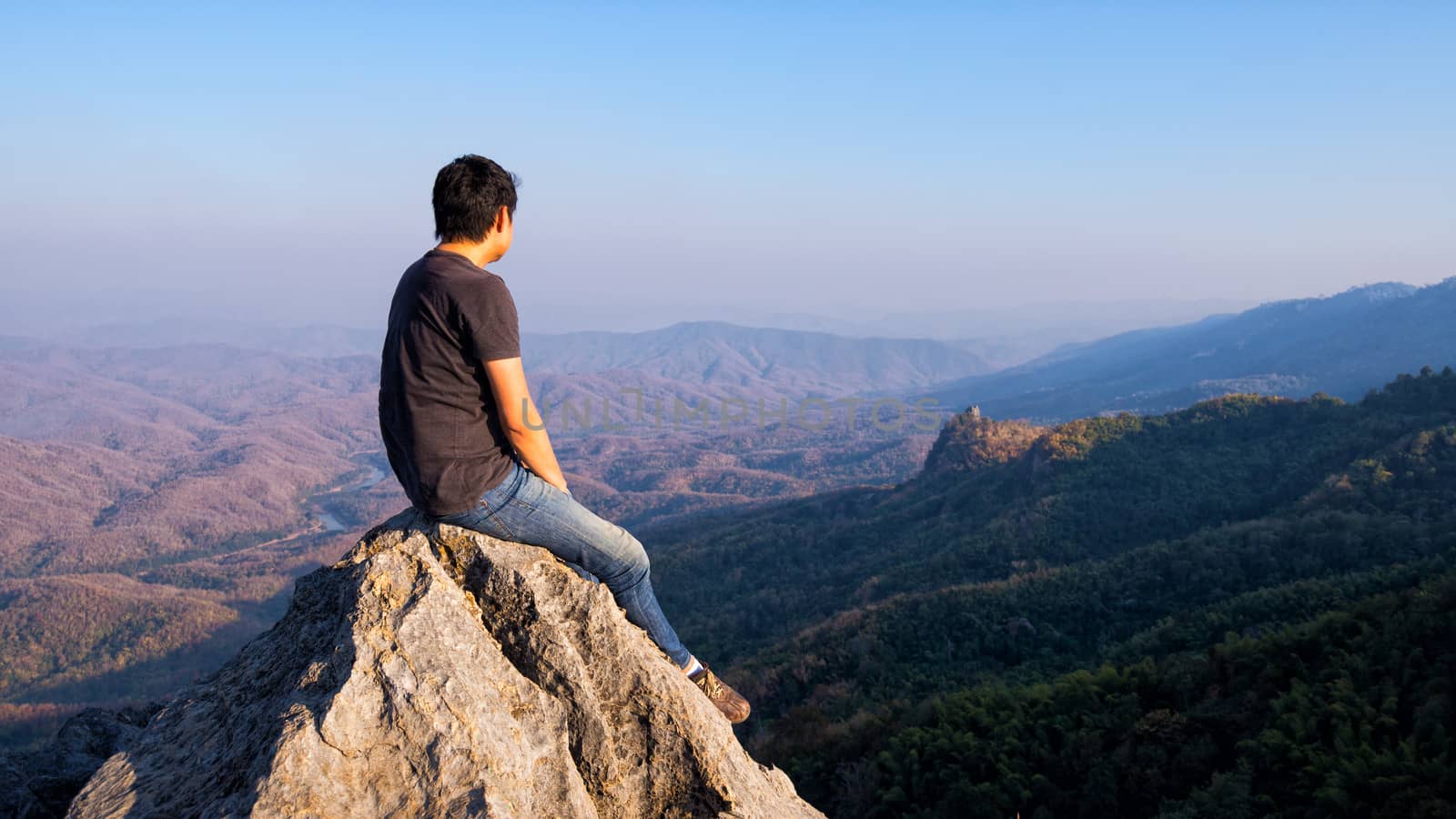 man sitting on stone top of high mountain