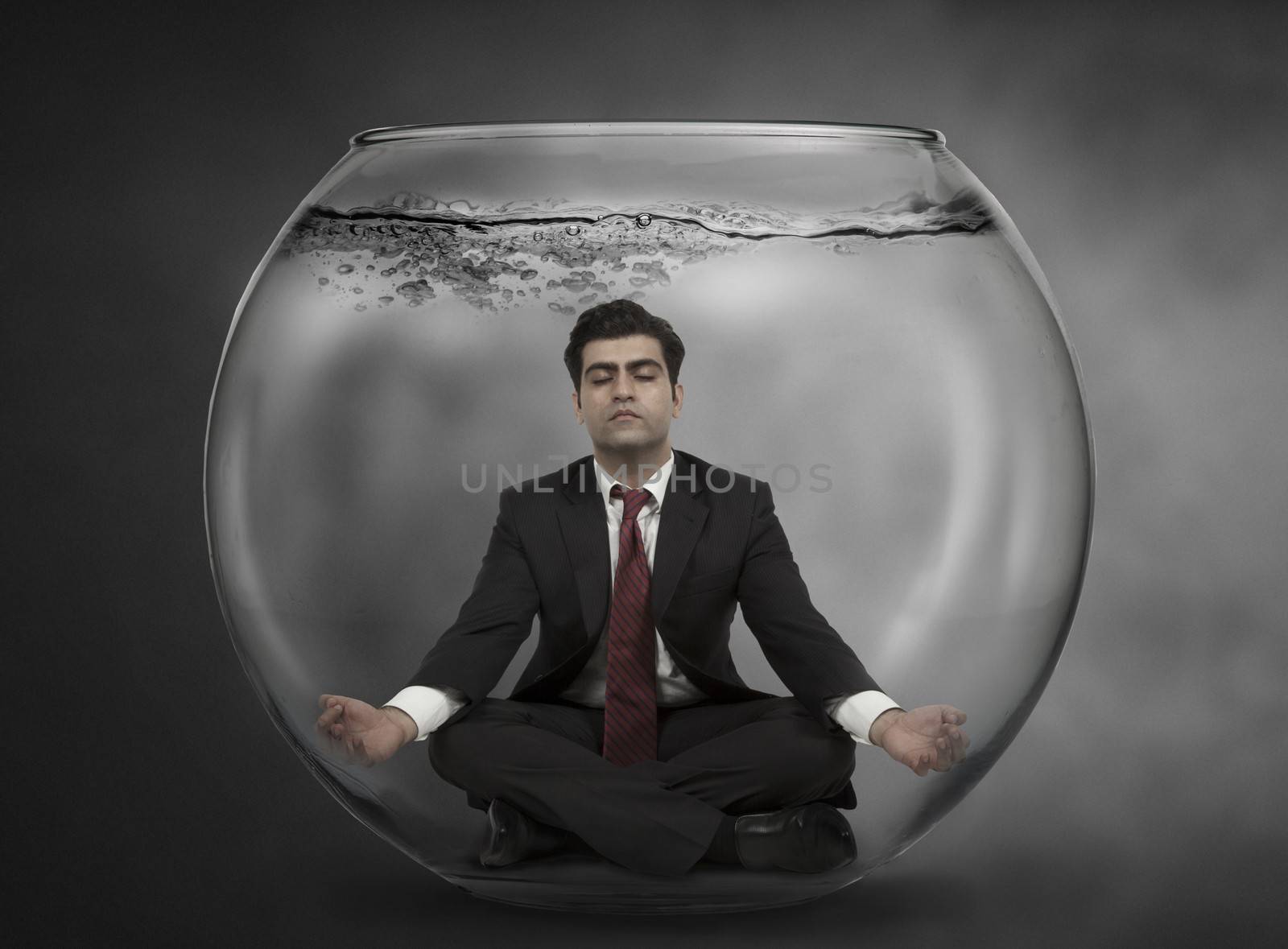 Business man meditates under water in a fish bowl 