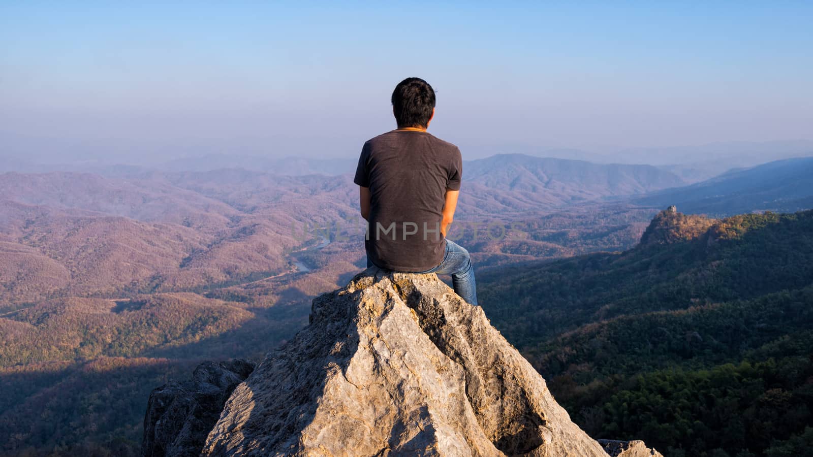 man sitting on stone top of high mountain