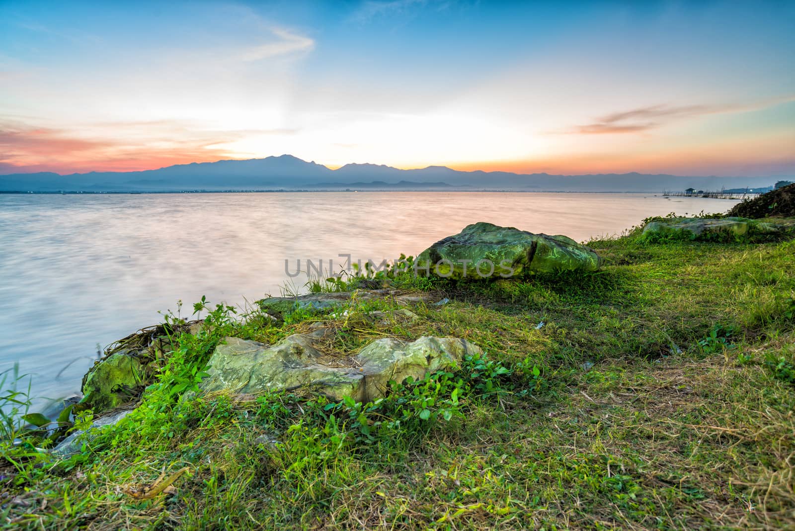 twilight time sunset behind mountain with lagoon  stone and grass in front of view motion blur of water in thailand