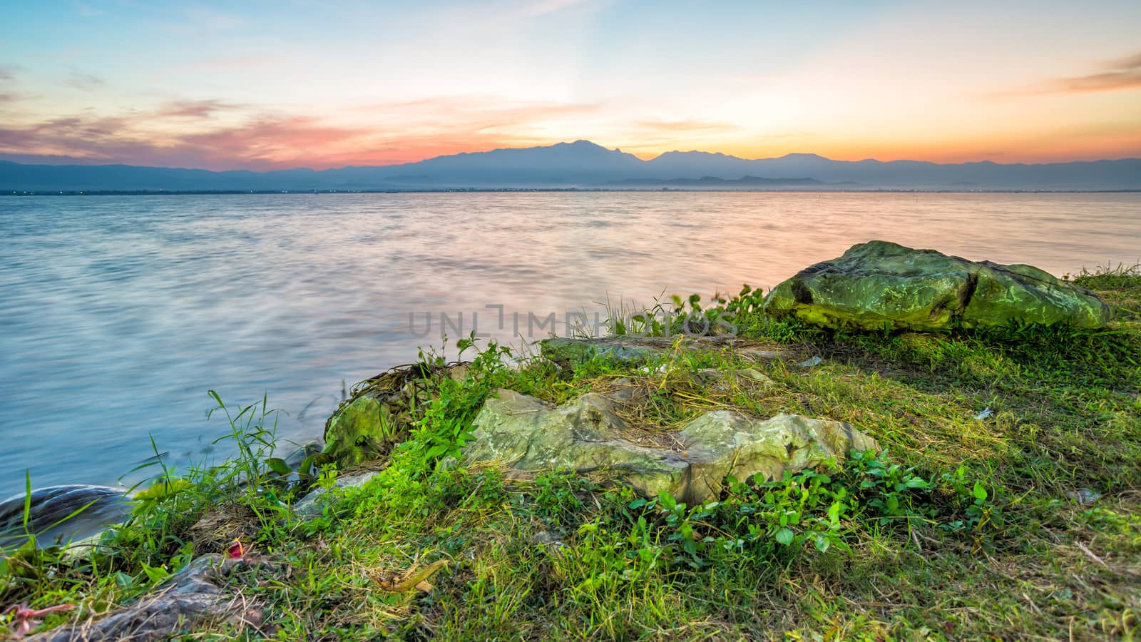 twilight time sunset behind mountain with lagoon  stone and grass in front of view motion blur of water in thailand