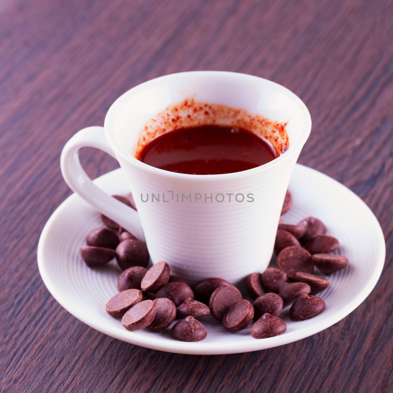 Hot Chocolate in small white cup with chocolate beans, over wooden background