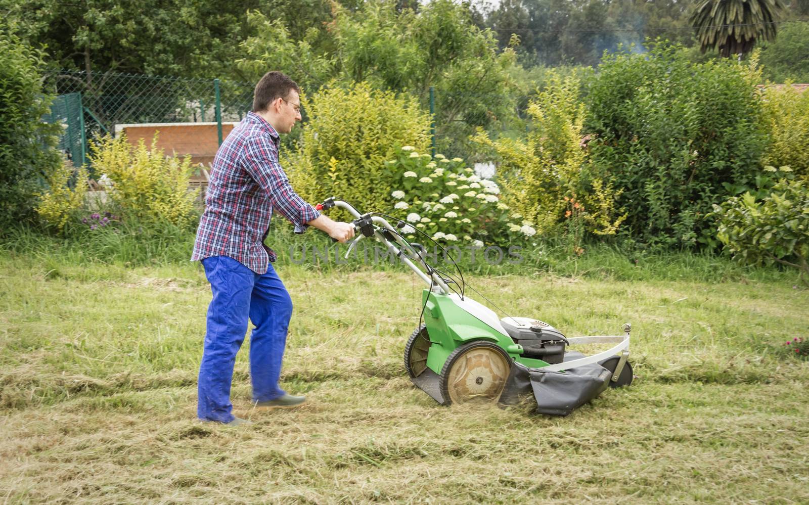 Young man mowing the lawn with a lawnmower machine