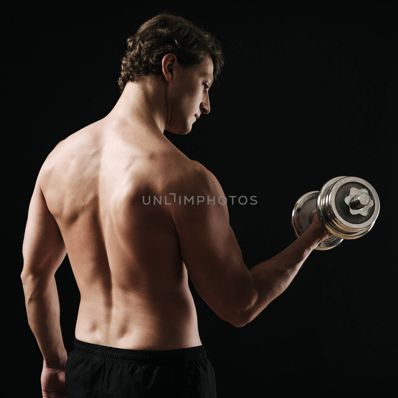 Photo of a man in his early thirties doing bicep curls with a dumbbell over a dark background. Rear view version.