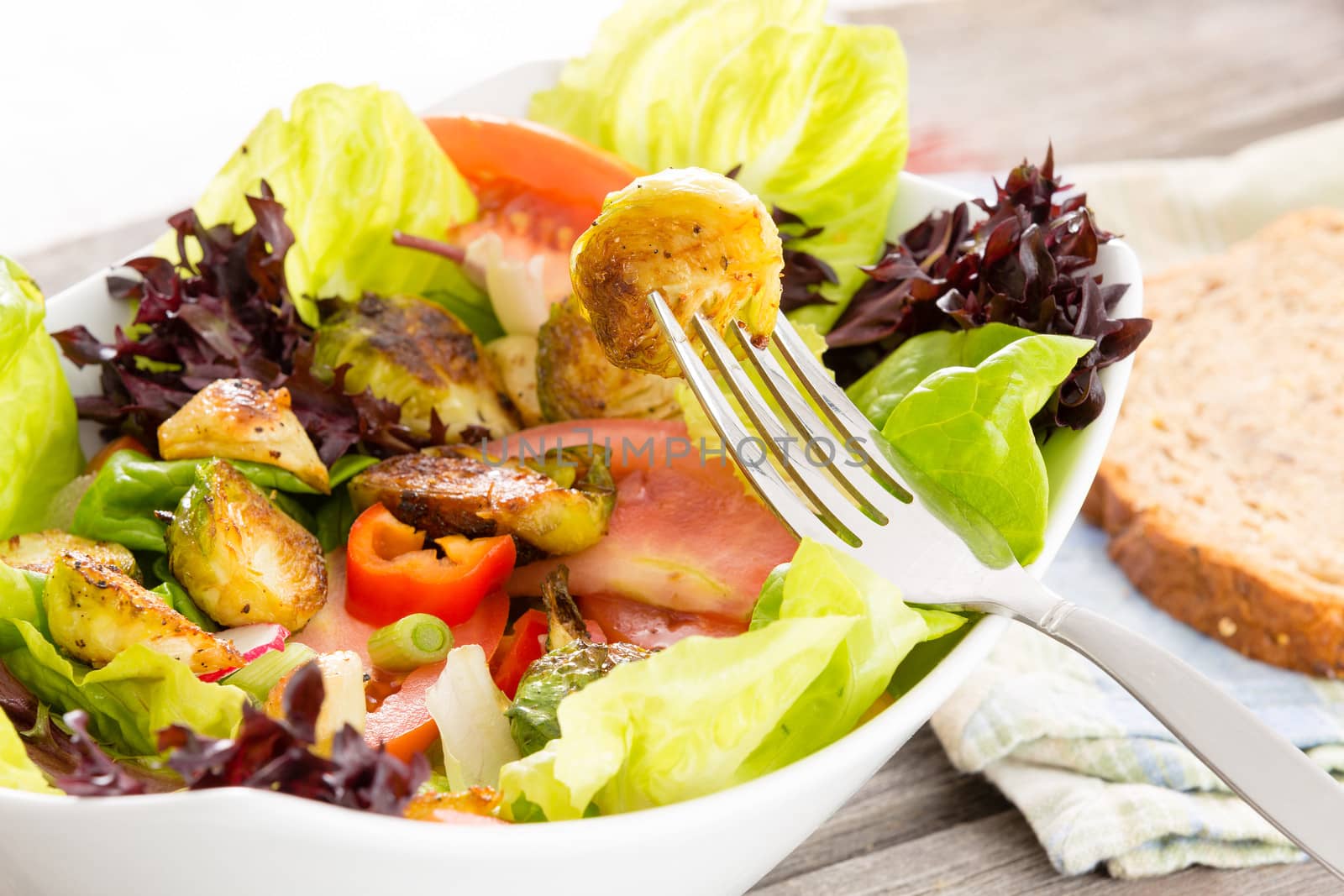 Enjoying a healthy vegetarian meal of sauteed brussels sprouts in a salad of leafy mixed greens, tomato and radish with a slice of wholewheat bread