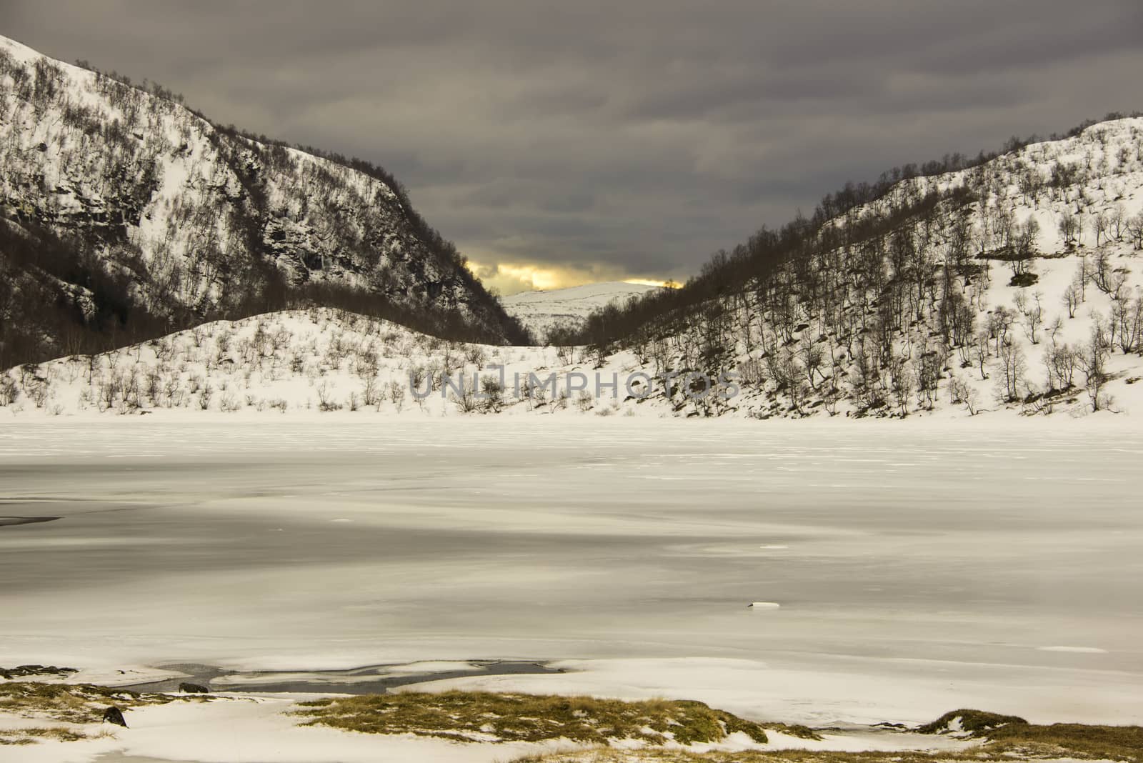 Winter landscape with snow, a frozen lake and a sunset far away