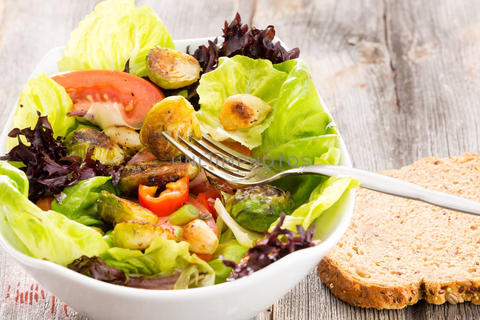 Sauteed brussels sprouts in a mixed leafy green salad with tomato being eaten with a slice of fresh brown bread for an enjoyable light healthy lunchtime meal