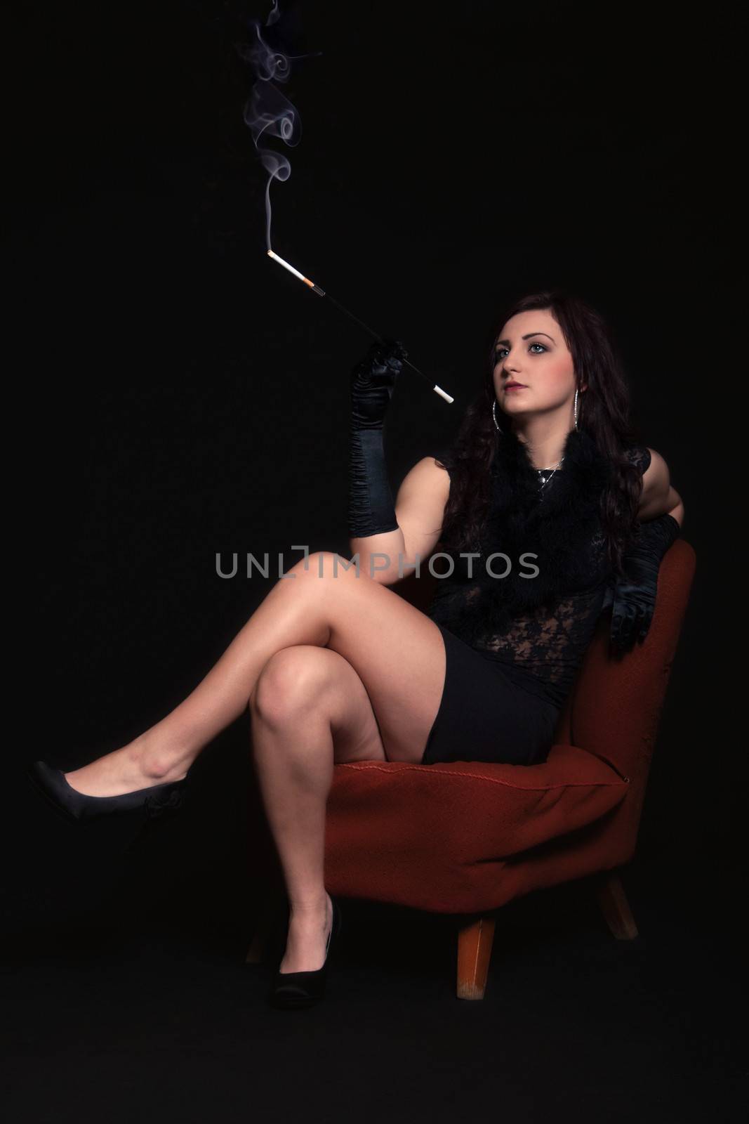 Young woman in retro clothes with cigarette sitting on old orange chair