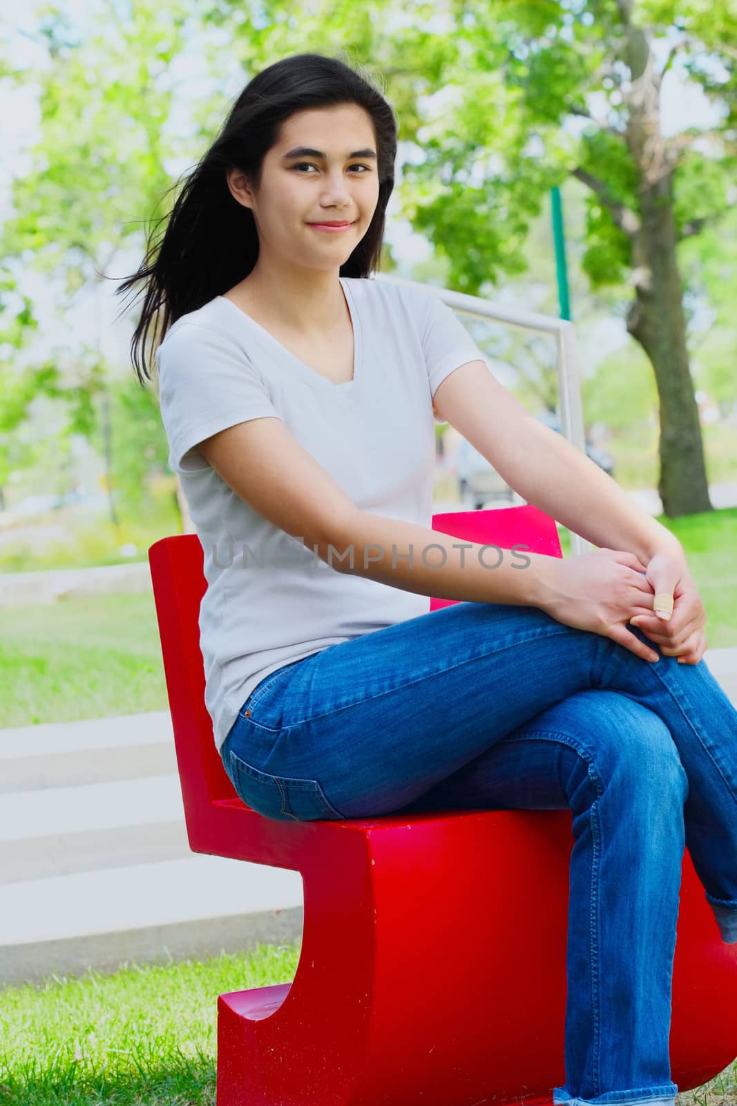 Beautiful biracial teen girl relaxing outdoors on red chair in summer