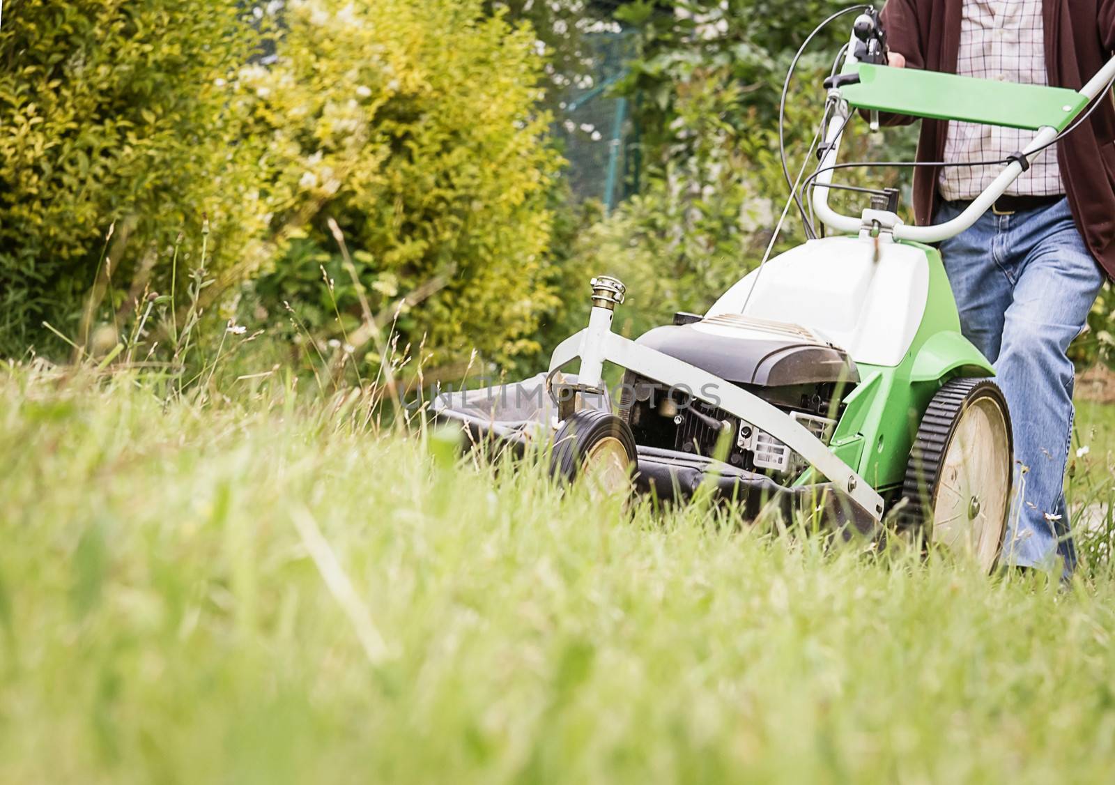 Senior man mowing the lawn with a lawnmower machine