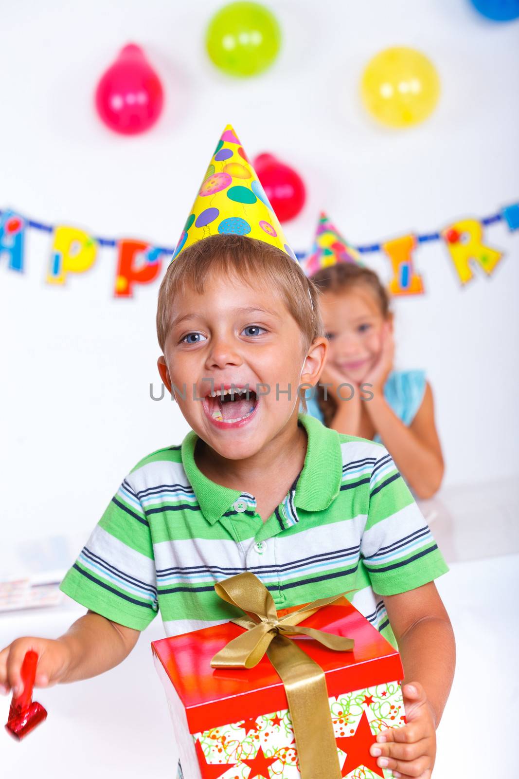 Handsome boy with giftbox looking at camera having fun at birthday party with his friends on background