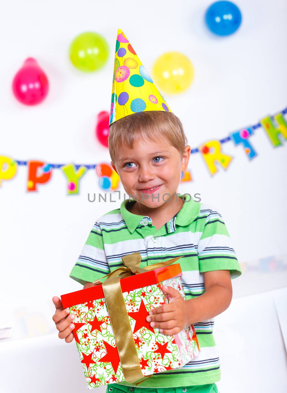 Handsome boy with giftbox looking at camera having fun at birthday party with his friends on background