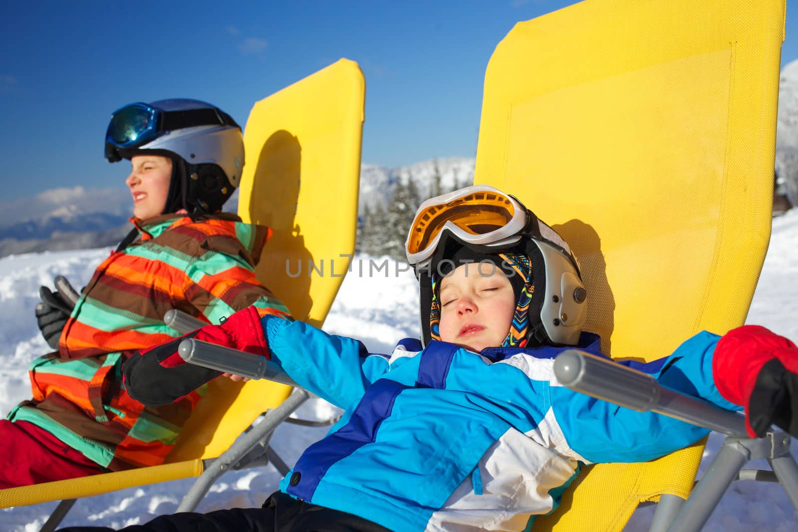 Winter, ski, sun and fun - portrait of kids in winter resort resting in the deck chair