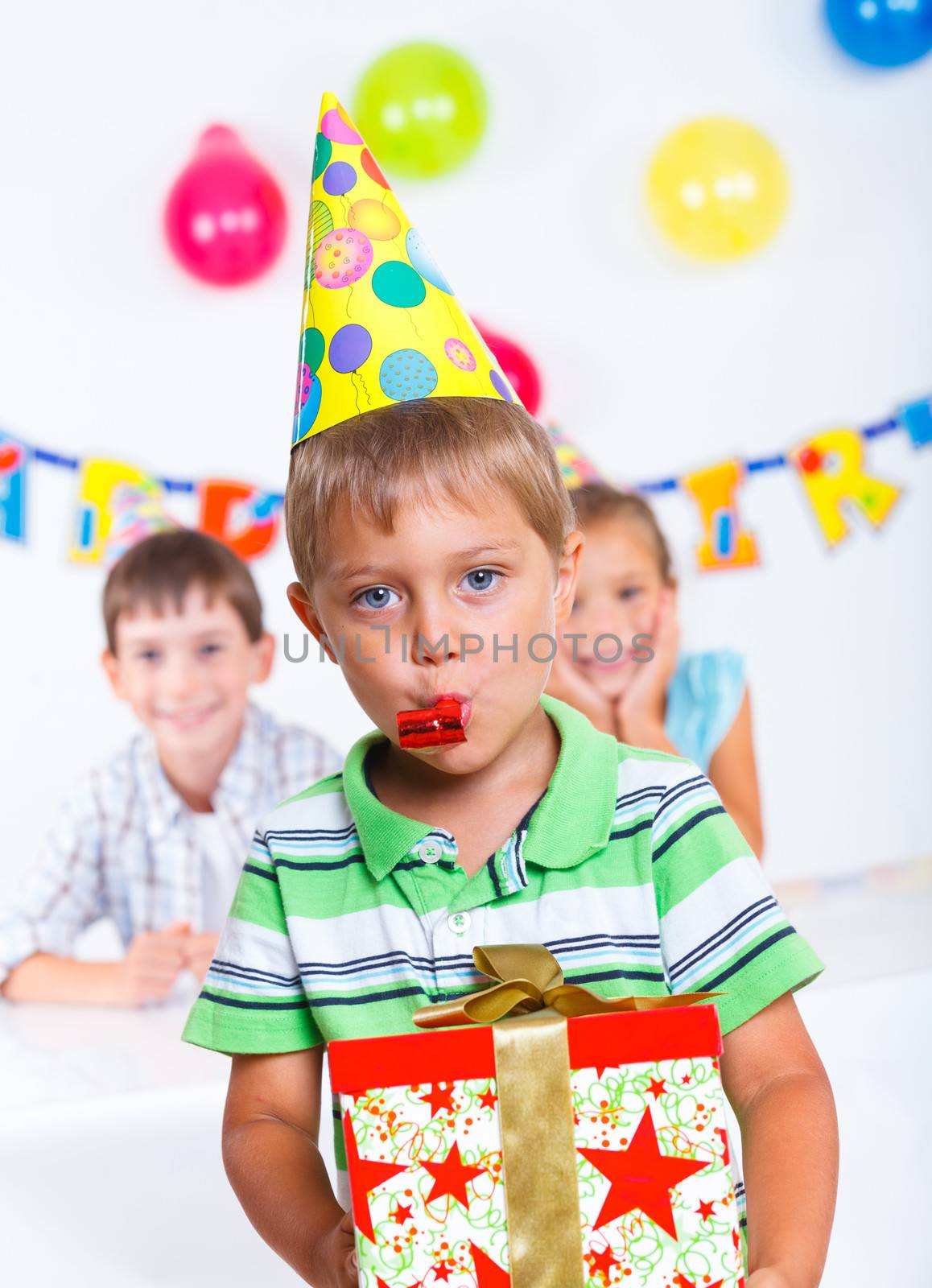 Handsome boy with giftbox looking at camera having fun at birthday party with his friends on background