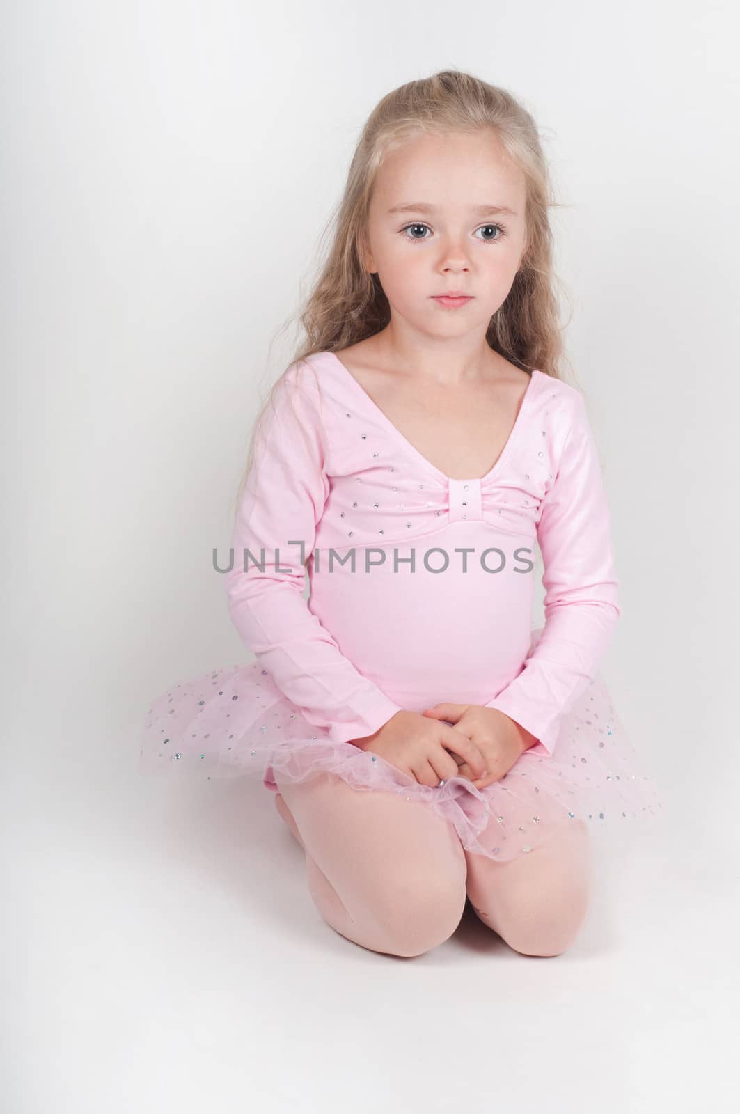 Studio shot of ballet dancer girl in pink sitting on the floor