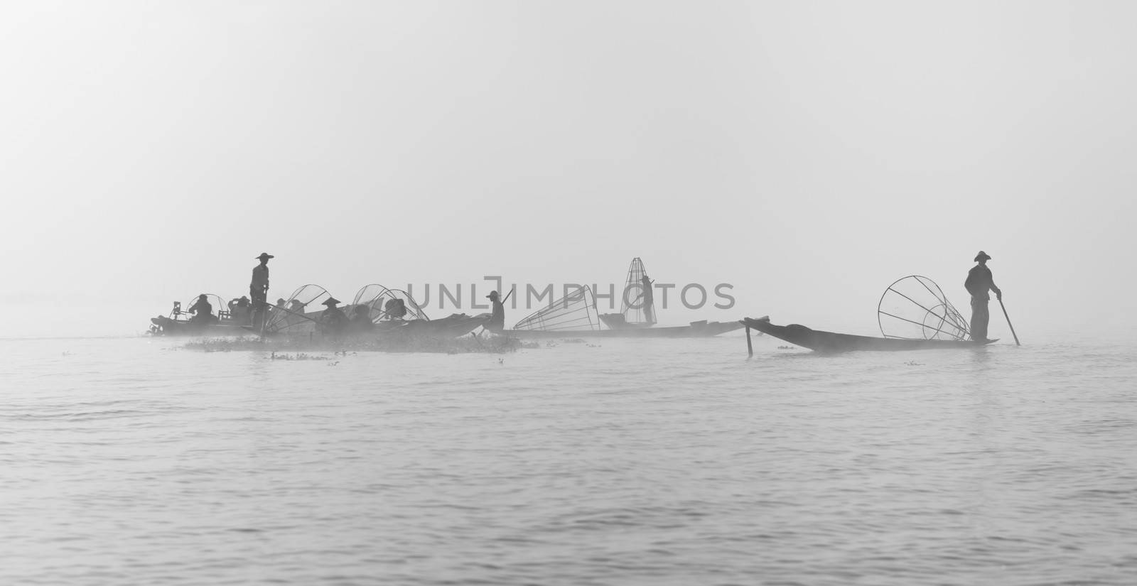 Foggy morning weather on a lake with silhouette of fishermen in small wooden boat 