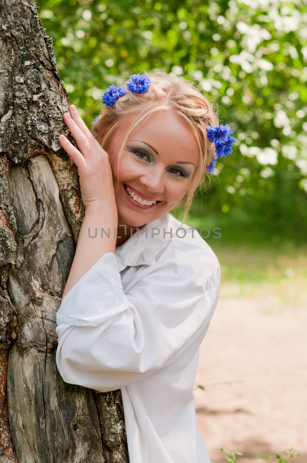 Smiling female in wreath from blue flowers near the tree