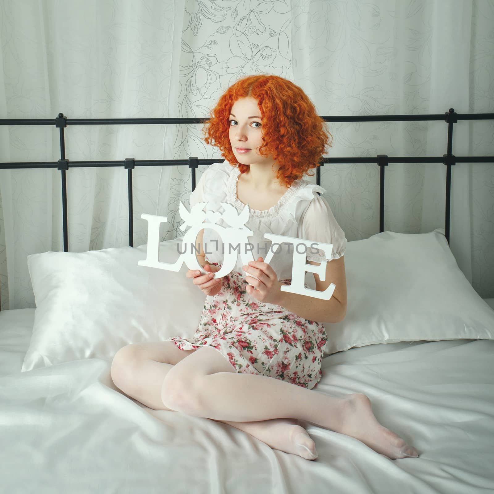 Attractive red-haired girl in a bedroom on the bed holding a love