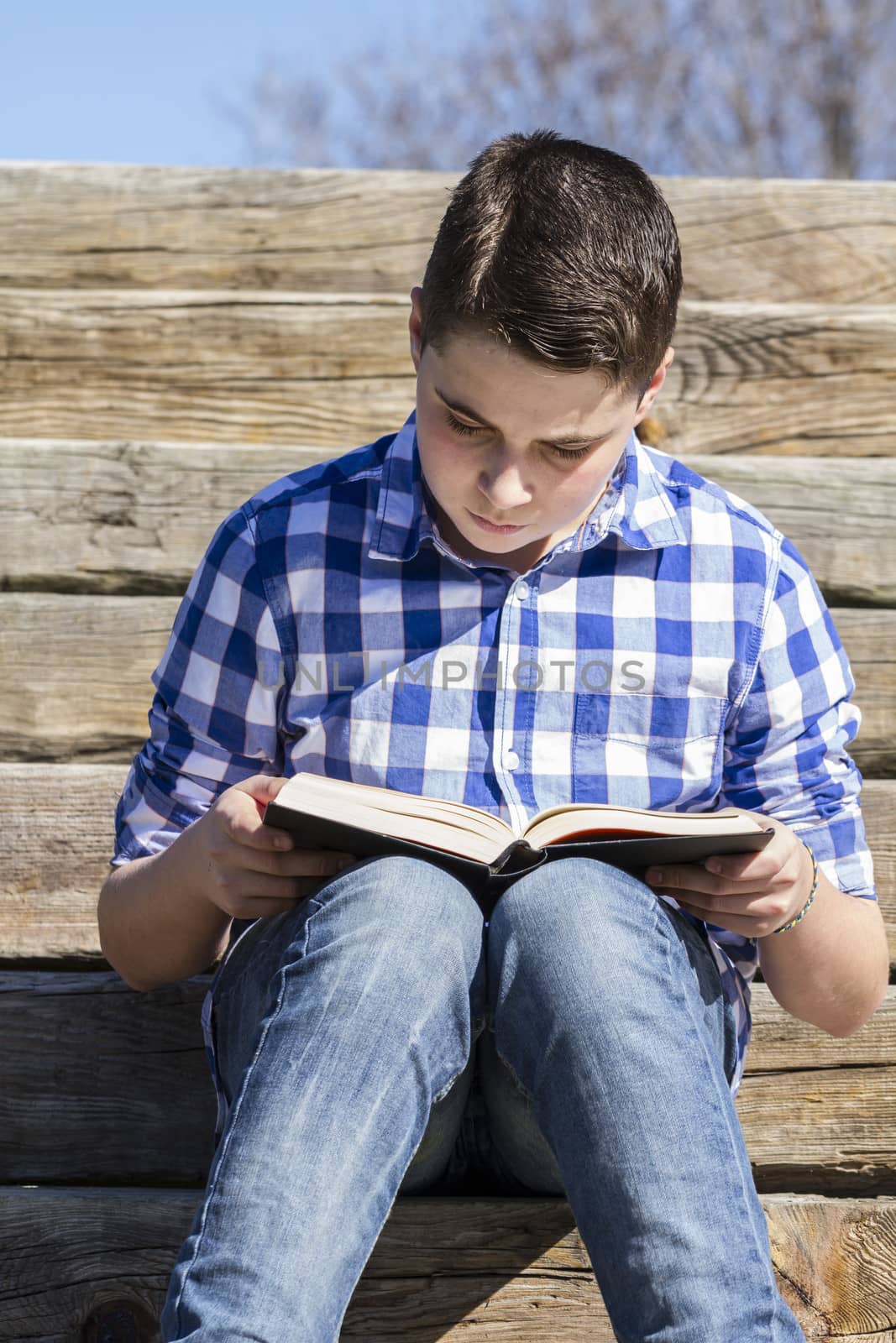 Learn.Young boy reading a book in the woods with shallow depth of field and copy space