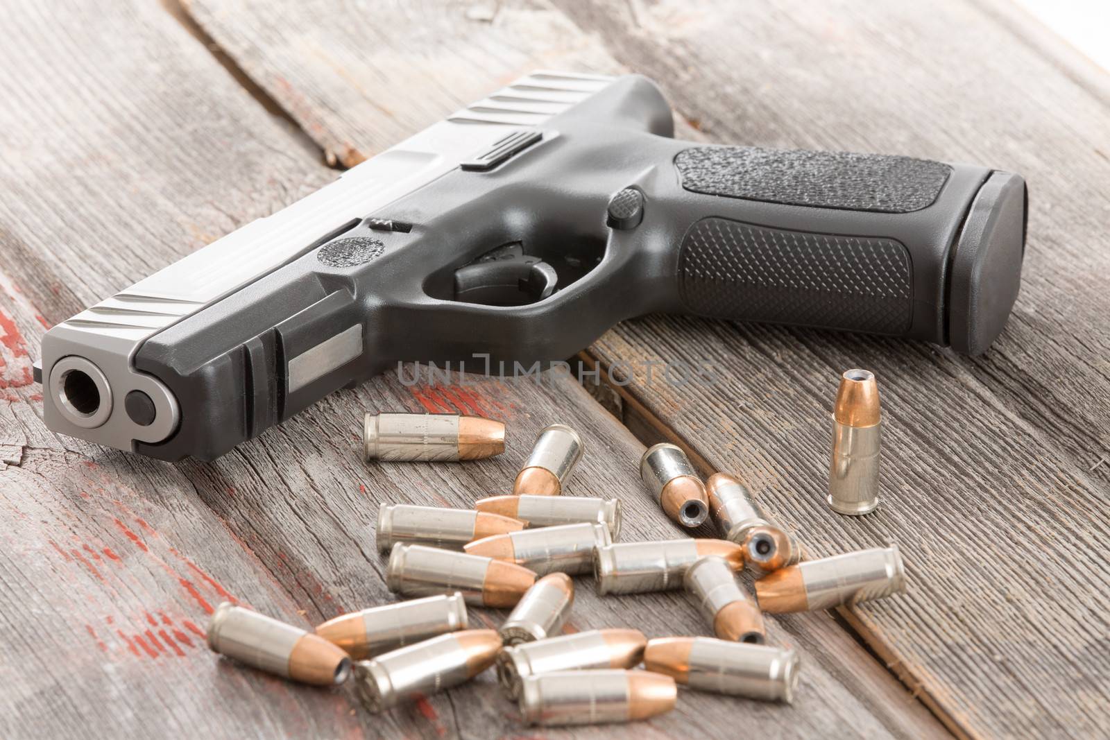 Handgun and a pile of scattered bullets lying on an old rustic wooden table conceptual of crime, violence, killing, coercion and protection of assets