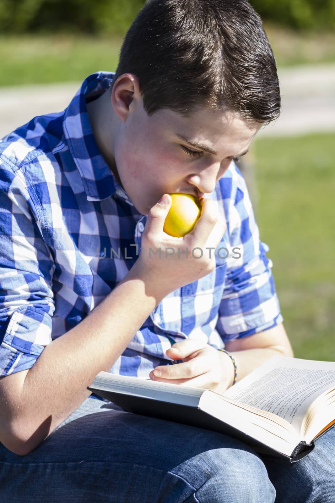 Summer.Young man reading a book in outdoor with yellow apple.