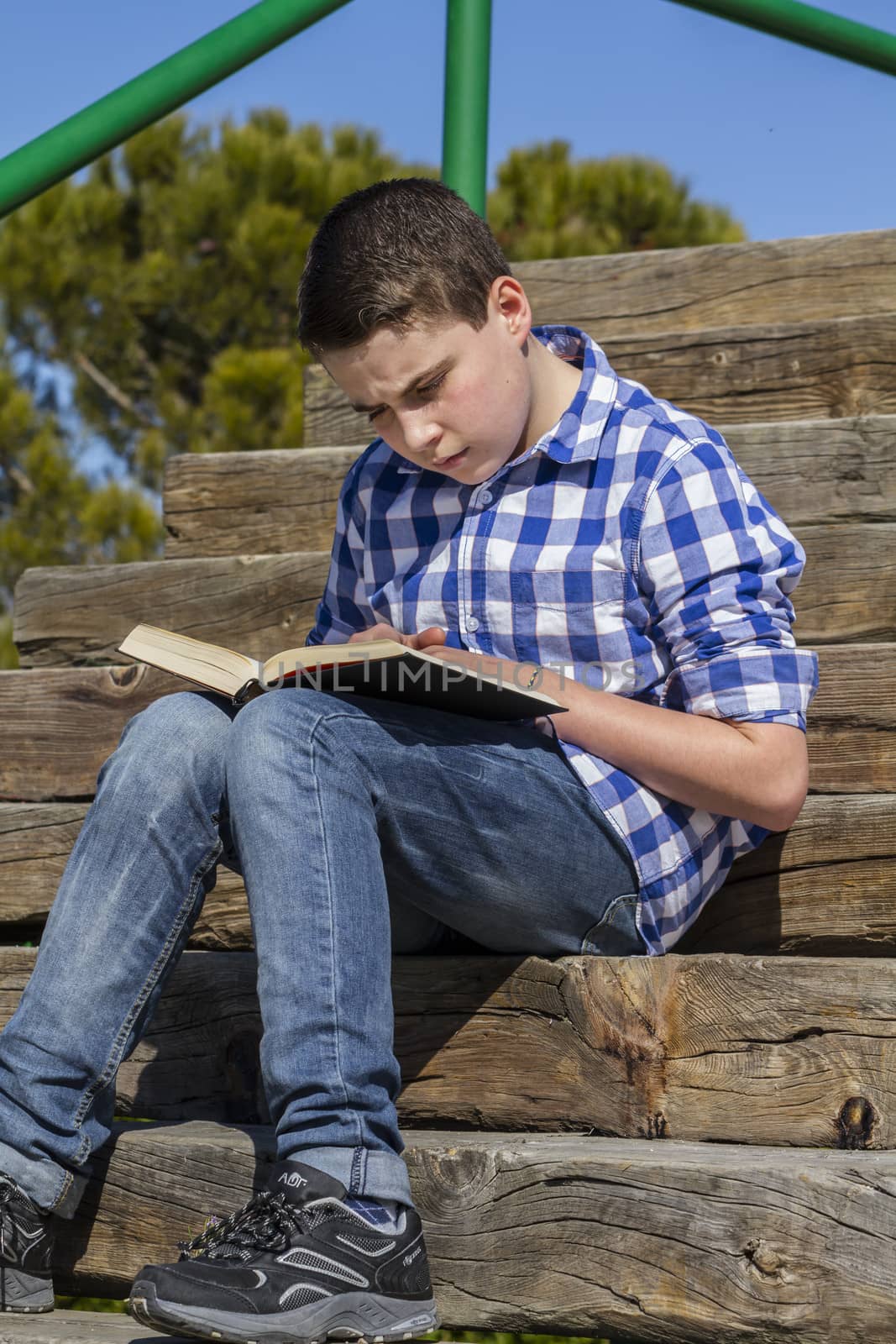 Young boy reading a book in wooden stairs, summer