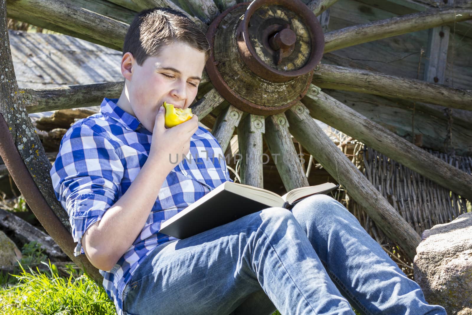 Relax.Young boy reading a book in the woods eating an apple
