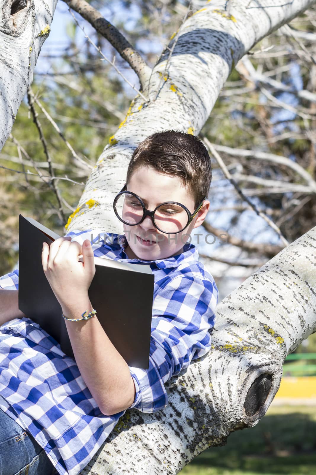 School.Huge glasses.Student boy reading a book in the woods with shallow depth of field and copy space
