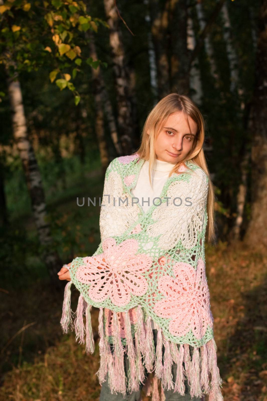 A standing blonde girl in a swal and jeans in a forest
