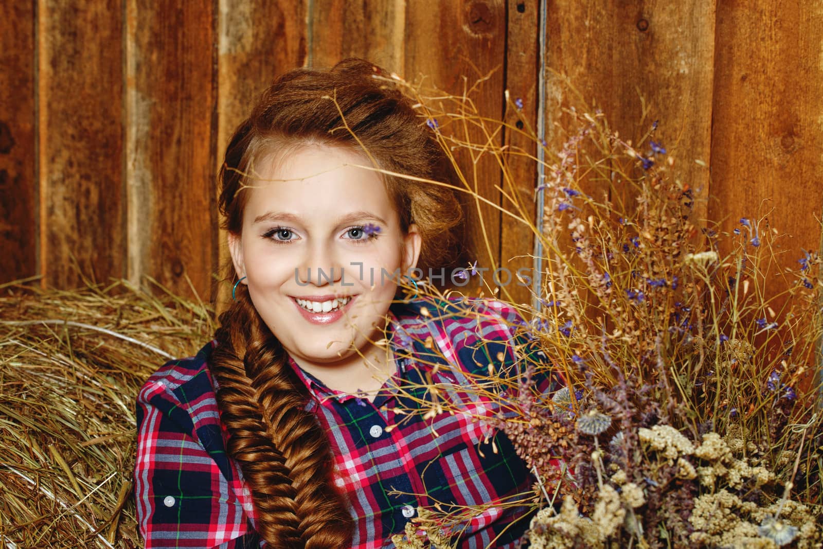 Cute little girl with a plait in a  lumberjack shirt in a rustic barn