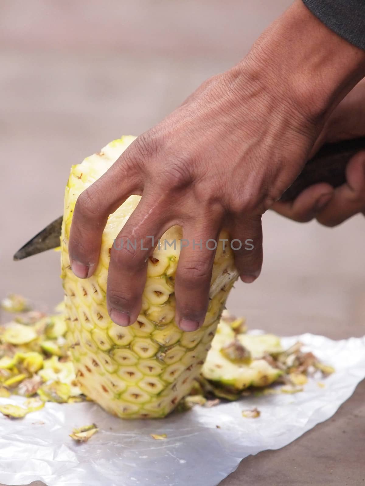Cropped view of an Asian woman slicing a pineapple with a knife      