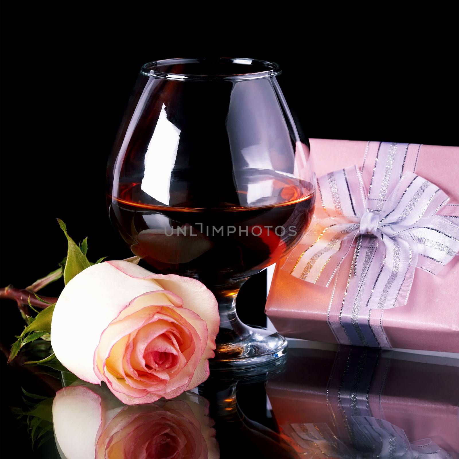 Glass and rose and gift box. Alcohol and flower and gift. Glass with drink and a pink rose and gift.